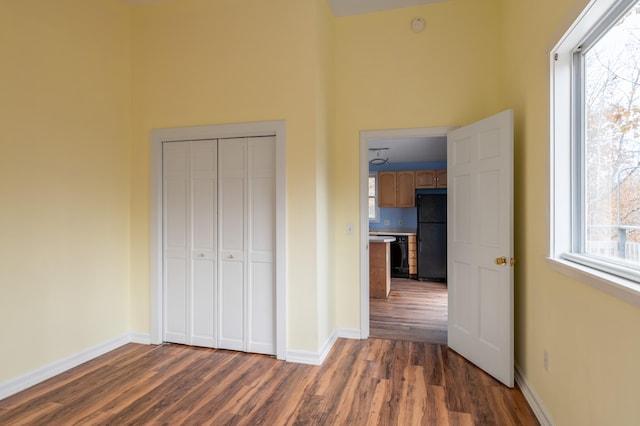 unfurnished bedroom with black fridge, dark wood-type flooring, and a closet