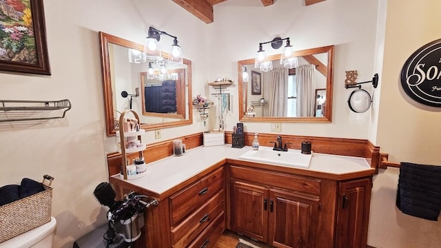 bathroom with beamed ceiling, vanity, and toilet