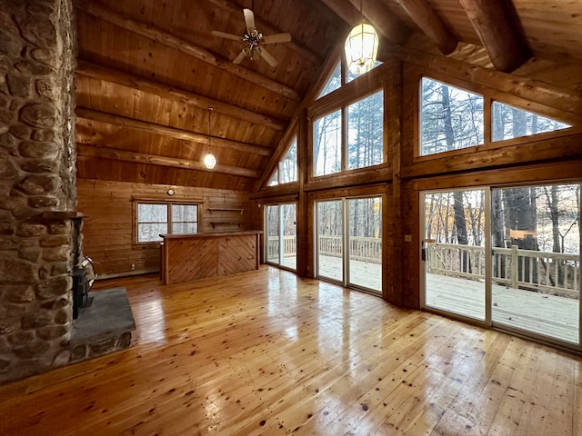 unfurnished living room featuring wood walls, wooden ceiling, light hardwood / wood-style flooring, ceiling fan, and beam ceiling