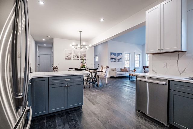 kitchen with stainless steel appliances, tasteful backsplash, hanging light fixtures, a notable chandelier, and dark hardwood / wood-style flooring