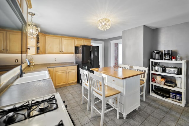 kitchen with freestanding refrigerator, light brown cabinets, a sink, and an inviting chandelier