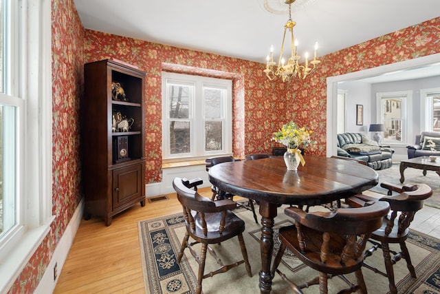 dining room with light wood-type flooring, visible vents, an inviting chandelier, and wallpapered walls