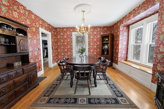 dining area featuring wallpapered walls, a notable chandelier, baseboards, and light wood-style floors