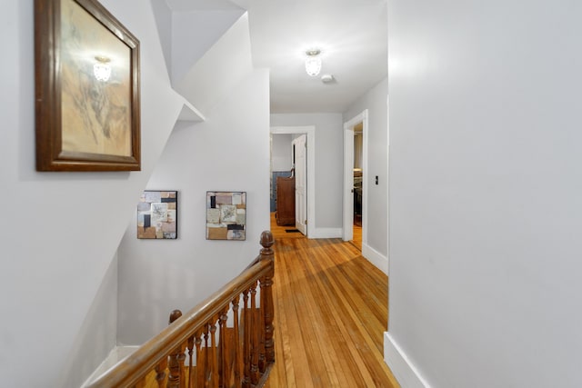 hall featuring light wood-style floors, baseboards, and an upstairs landing