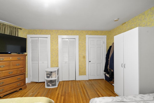 bedroom featuring light wood finished floors, multiple closets, and wallpapered walls