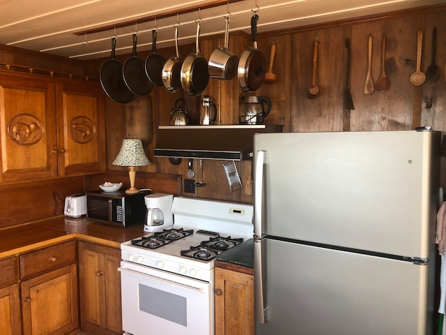 kitchen featuring white range with gas stovetop, ventilation hood, and stainless steel refrigerator