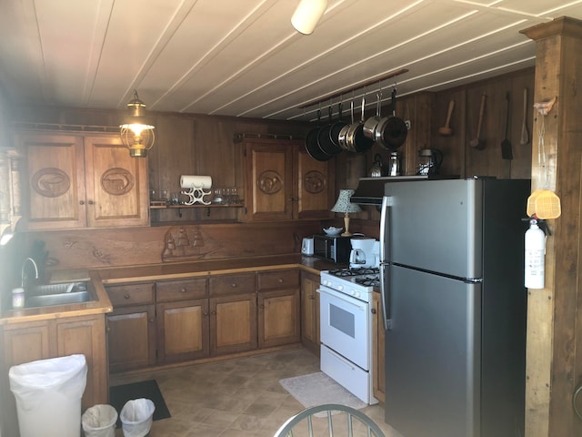 kitchen featuring stainless steel fridge, white range with gas cooktop, wooden walls, and sink