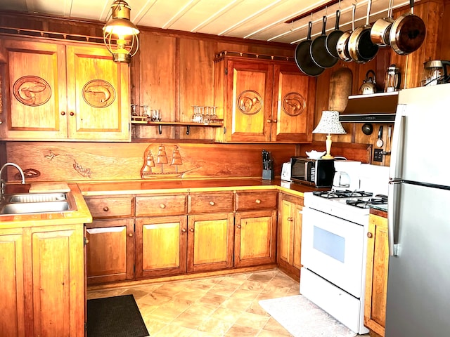 kitchen featuring wood walls, sink, white range with gas stovetop, and fridge