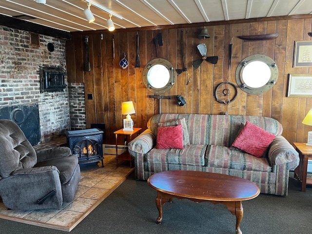 carpeted living room with rail lighting, brick wall, a baseboard heating unit, a wood stove, and wood walls