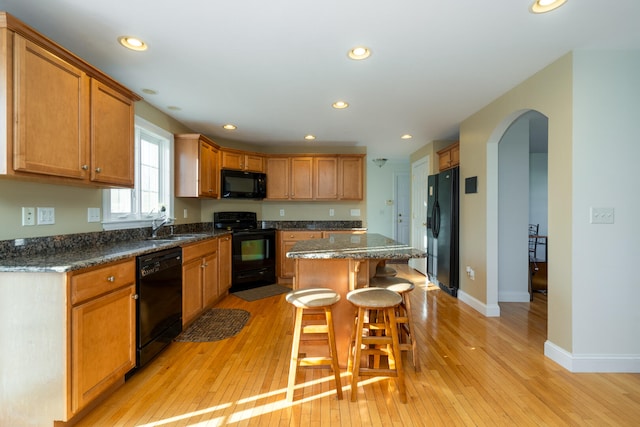 kitchen featuring dark stone countertops, a kitchen island, black appliances, and light wood-type flooring