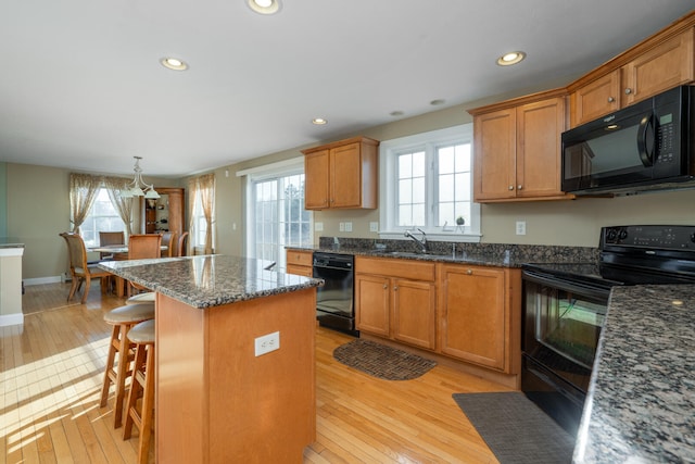 kitchen with a healthy amount of sunlight, a center island, black appliances, and light hardwood / wood-style floors