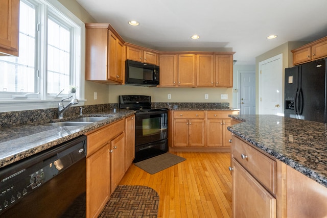 kitchen with sink, light hardwood / wood-style floors, dark stone counters, and black appliances