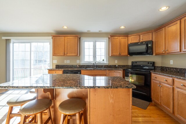 kitchen featuring light wood-type flooring, sink, black appliances, a center island, and a breakfast bar area