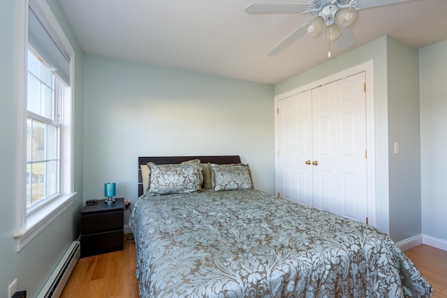 bedroom with hardwood / wood-style flooring, ceiling fan, a baseboard heating unit, and a closet