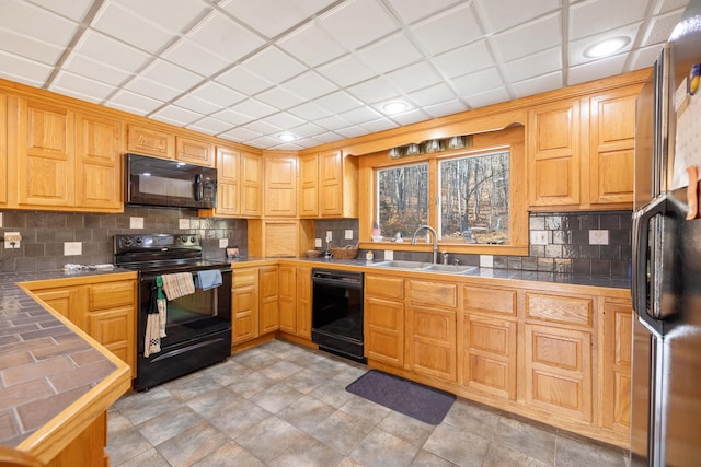 kitchen with a paneled ceiling, sink, black appliances, tile counters, and decorative backsplash