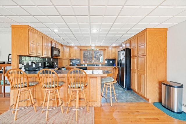 kitchen featuring a kitchen breakfast bar, black appliances, kitchen peninsula, and light wood-type flooring