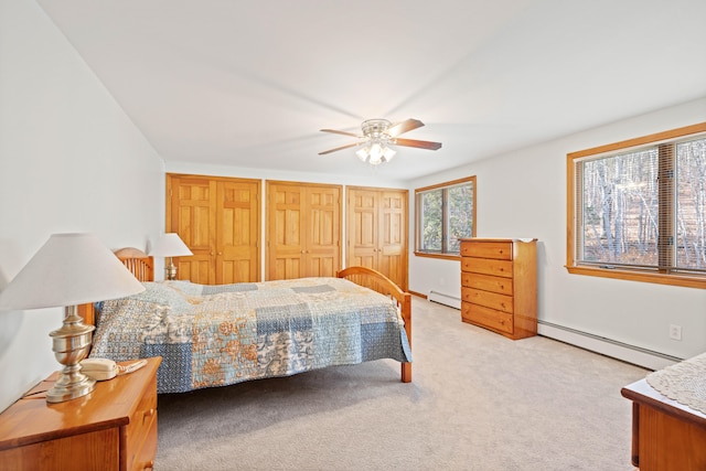 carpeted bedroom with ceiling fan, multiple closets, and a baseboard heating unit