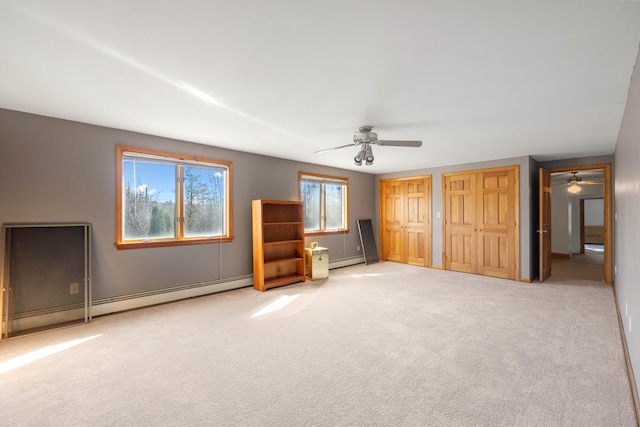 unfurnished bedroom featuring baseboard heating, light carpet, two closets, and ceiling fan