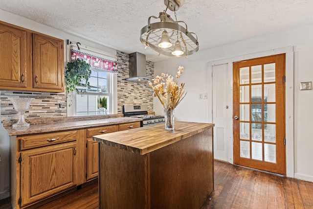 kitchen with dark wood-type flooring, stainless steel gas range, wall chimney range hood, and a center island