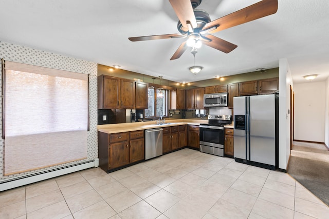 kitchen with a baseboard heating unit, stainless steel appliances, sink, ceiling fan, and light tile patterned flooring