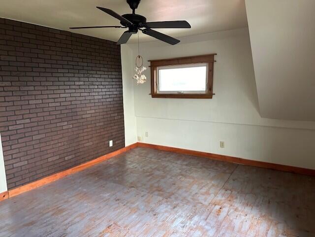 unfurnished room with hardwood / wood-style flooring, ceiling fan, and brick wall