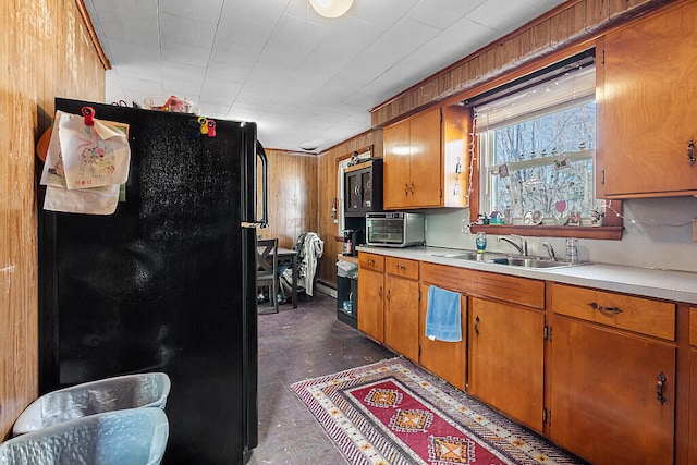 kitchen featuring black refrigerator, wood walls, and sink