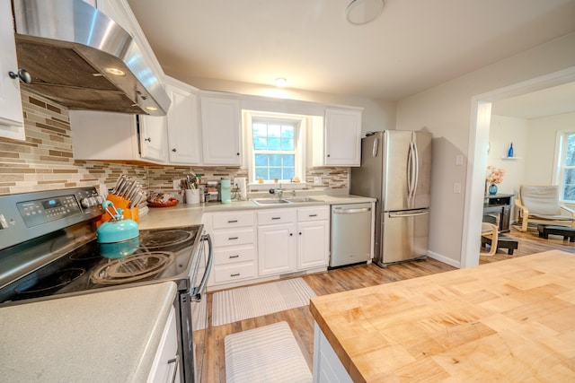 kitchen featuring appliances with stainless steel finishes, backsplash, light hardwood / wood-style flooring, white cabinets, and range hood