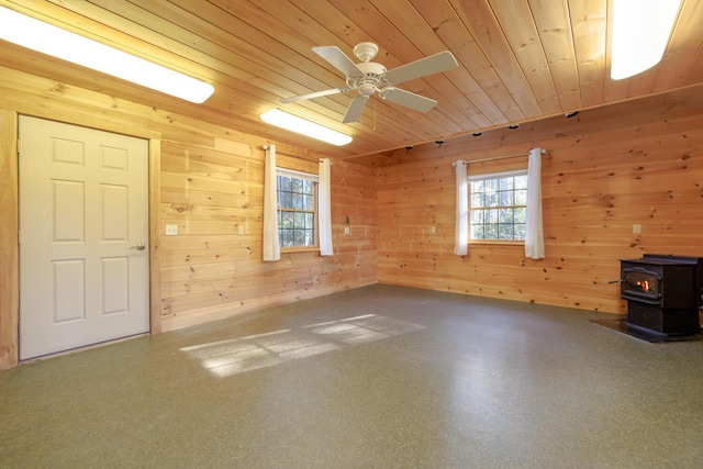 spare room with ceiling fan, a wood stove, wood ceiling, and wood walls