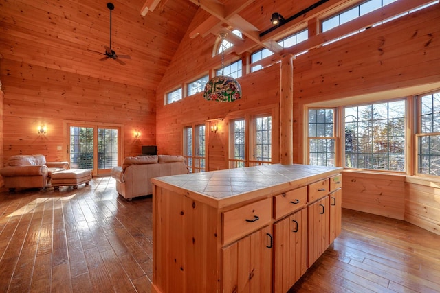 kitchen featuring wood walls, high vaulted ceiling, beamed ceiling, tile counters, and a kitchen island