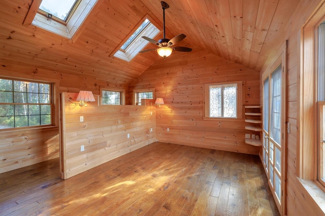 empty room featuring wood walls, vaulted ceiling with skylight, wood ceiling, and light wood-type flooring