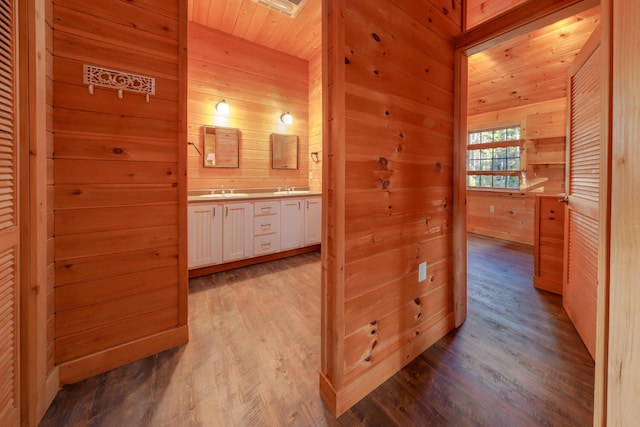 corridor with wooden walls, sink, wood ceiling, and light wood-type flooring