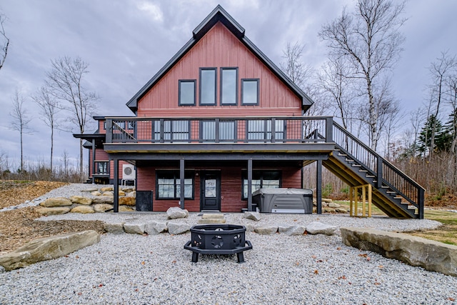 back of property with a deck, a hot tub, and a fire pit