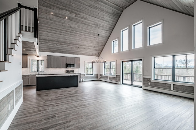 unfurnished living room with dark wood-type flooring, baseboard heating, an inviting chandelier, and high vaulted ceiling