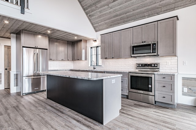 kitchen featuring stainless steel appliances, light hardwood / wood-style floors, light stone countertops, and a kitchen island