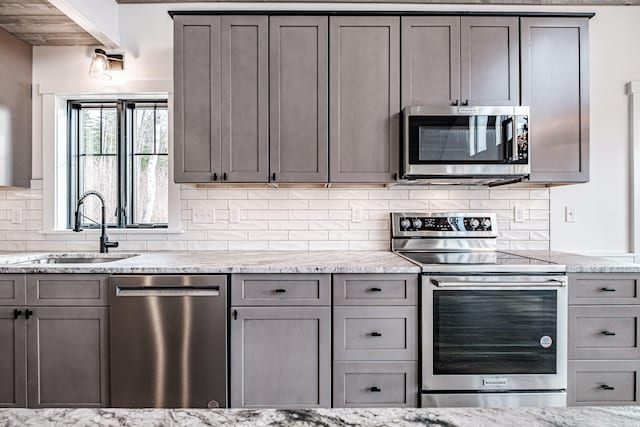 kitchen with tasteful backsplash, gray cabinetry, appliances with stainless steel finishes, light stone countertops, and sink