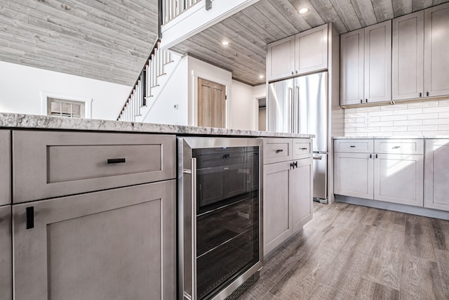 kitchen with wine cooler, light stone counters, hardwood / wood-style floors, gray cabinetry, and high end fridge