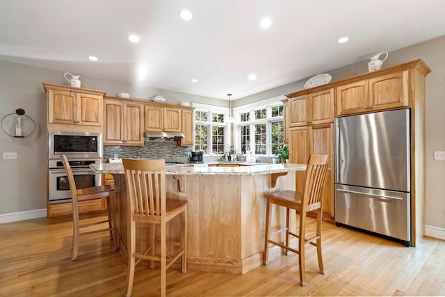 kitchen featuring light hardwood / wood-style floors, light stone counters, appliances with stainless steel finishes, a kitchen island, and a kitchen bar