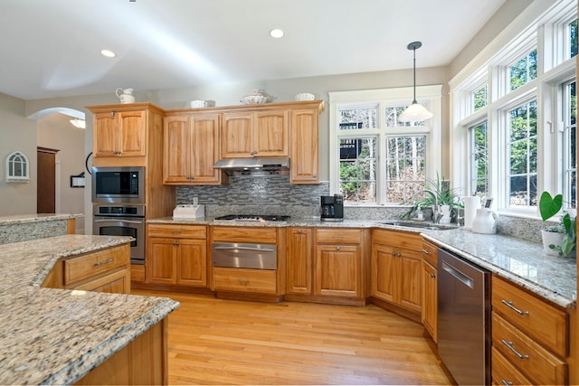 kitchen with light stone countertops, appliances with stainless steel finishes, backsplash, sink, and light hardwood / wood-style floors