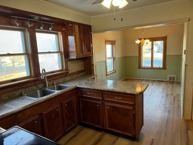 kitchen featuring kitchen peninsula, ornamental molding, sink, light hardwood / wood-style flooring, and hanging light fixtures