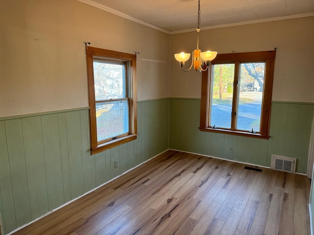 empty room with an inviting chandelier, light hardwood / wood-style flooring, ornamental molding, and wood walls