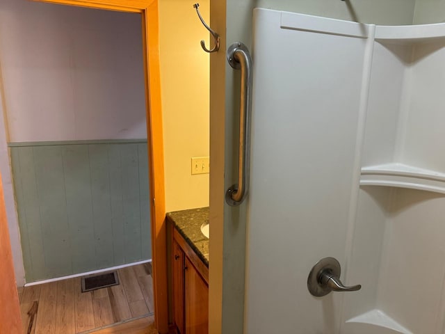 bathroom featuring hardwood / wood-style flooring, vanity, a shower, and wooden walls