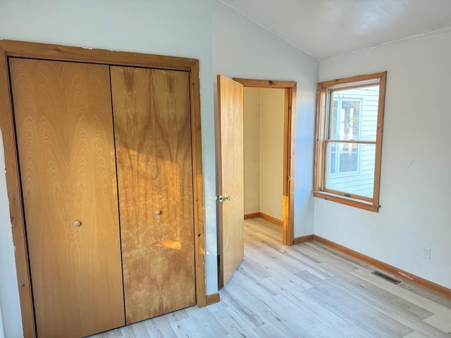 unfurnished bedroom with vaulted ceiling, light wood-type flooring, and a closet