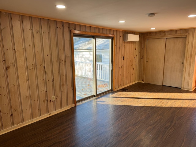 unfurnished room with wood-type flooring, a wall unit AC, and wooden walls