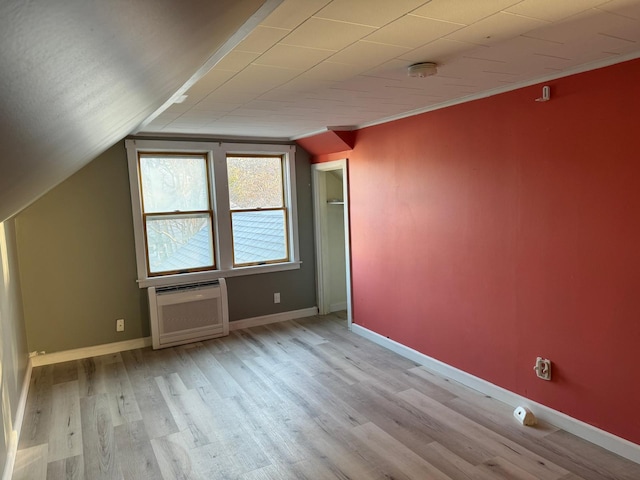 additional living space with light wood-type flooring, a wall mounted AC, and vaulted ceiling