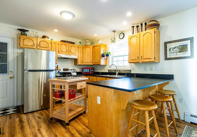 kitchen with kitchen peninsula, a kitchen bar, stainless steel appliances, sink, and hardwood / wood-style floors