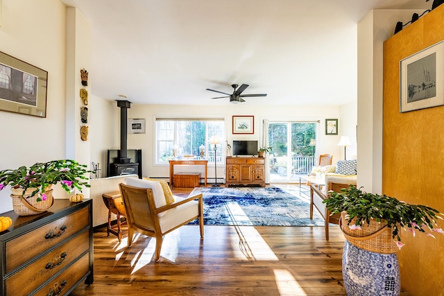 living room with a wood stove, ceiling fan, and dark wood-type flooring