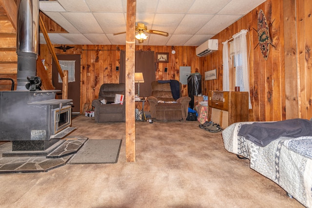 basement with a wood stove, ceiling fan, a drop ceiling, a wall mounted AC, and wood walls