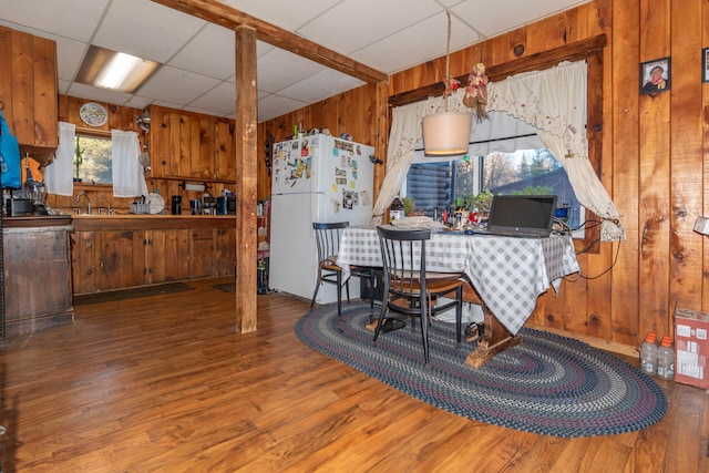 dining space featuring wooden walls, a drop ceiling, sink, and hardwood / wood-style flooring