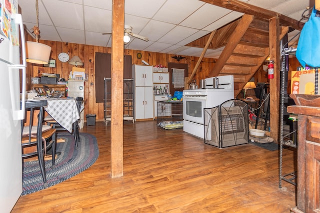 interior space with ceiling fan, a drop ceiling, wood walls, wood-type flooring, and white stove