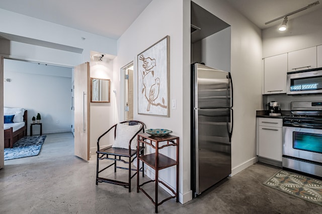 kitchen featuring white cabinets, rail lighting, appliances with stainless steel finishes, and concrete floors